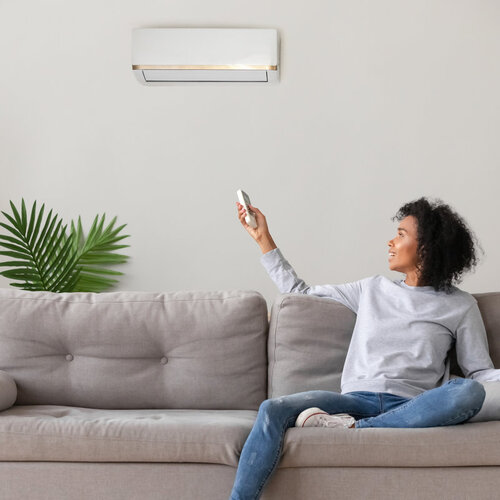 happy young woman turning on an air conditioner