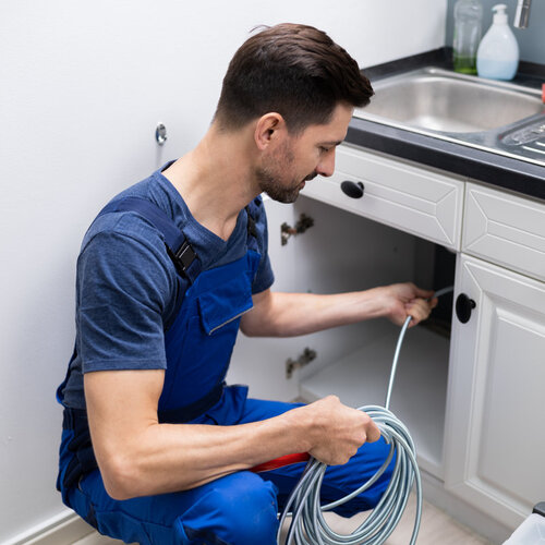 plumber providing drain cleaning beneath a sink